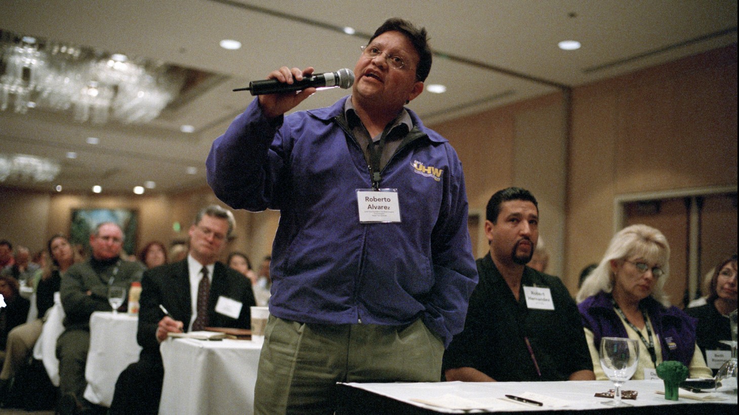 A UHW member (wearing purple jacket) speaks into a microphone
