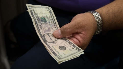 A man's hand holding a five dollar bill 