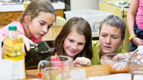 Two girls carefully measure cooking oil as their mentor looks on