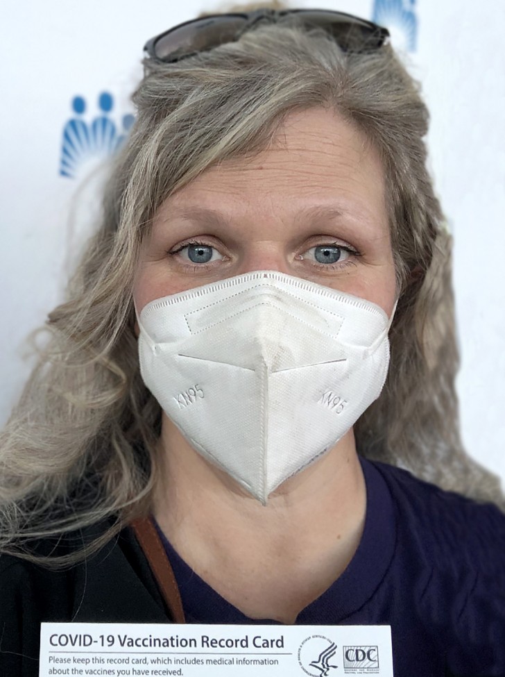 woman with blonde hair and blue eyes, wearing a white mask