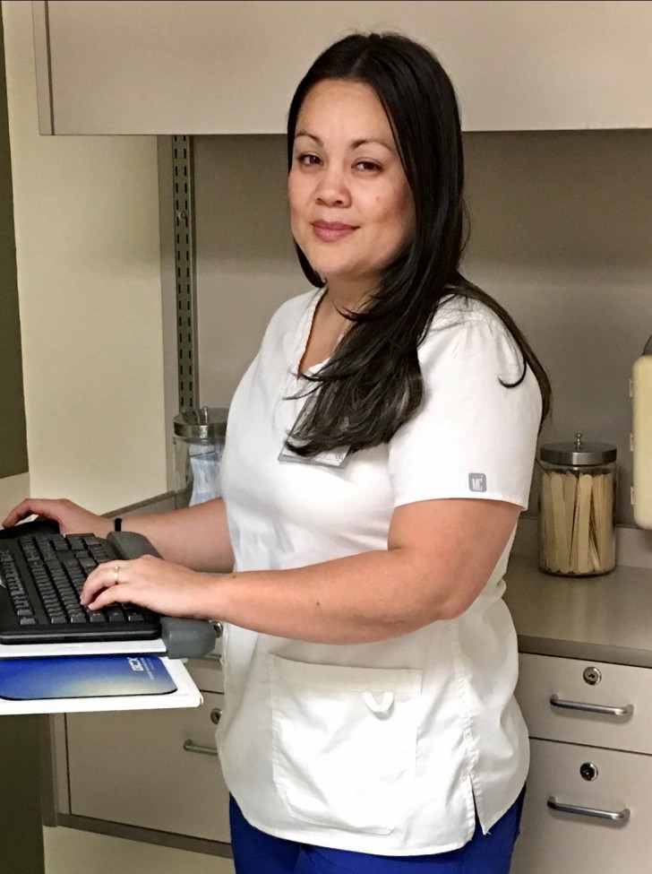 Female health care worker wearing white scrubs, standing at a computer keyboard