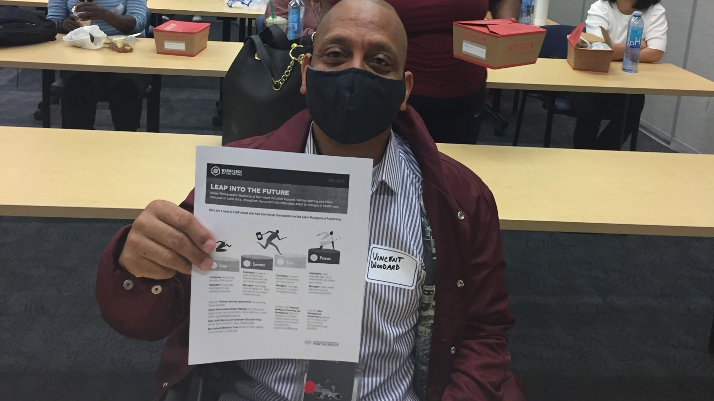 A black man, wearing a mask, holding up a flier